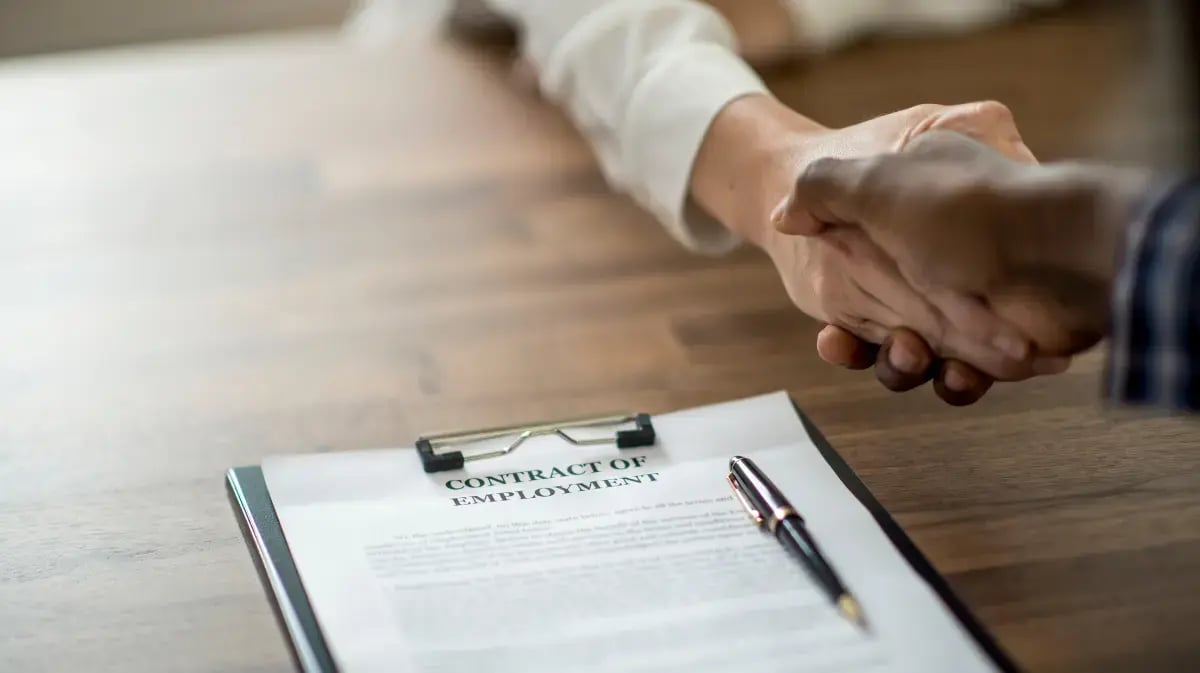 employment contract on a desktop with two people shaking hands